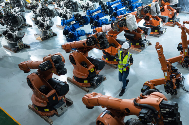 A female engineer installs a program on a robotics arm in a robot warehouse. And test the operation before sending the machine to the customer.