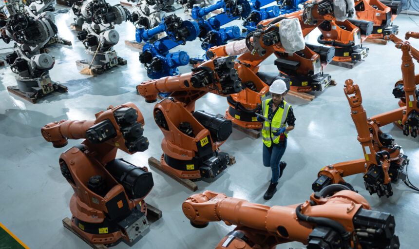 A female engineer installs a program on a robotics arm in a robot warehouse. And test the operation before sending the machine to the customer.