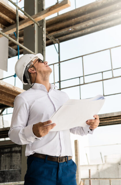 Young man architect or businessman wearing hard hat and holding blueprints on a construction site